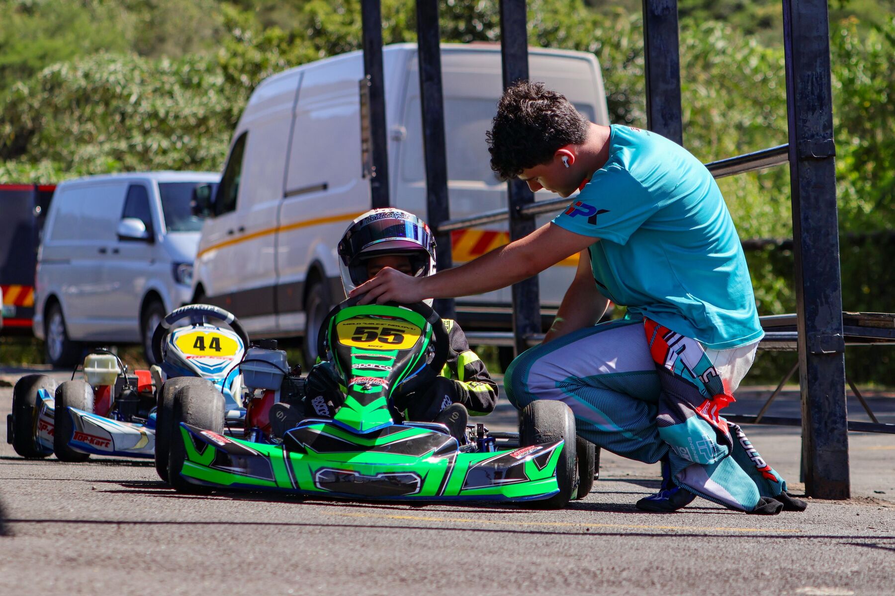 Jonno Wilson coaching a young karting driver trackside, adjusting helmet and setup